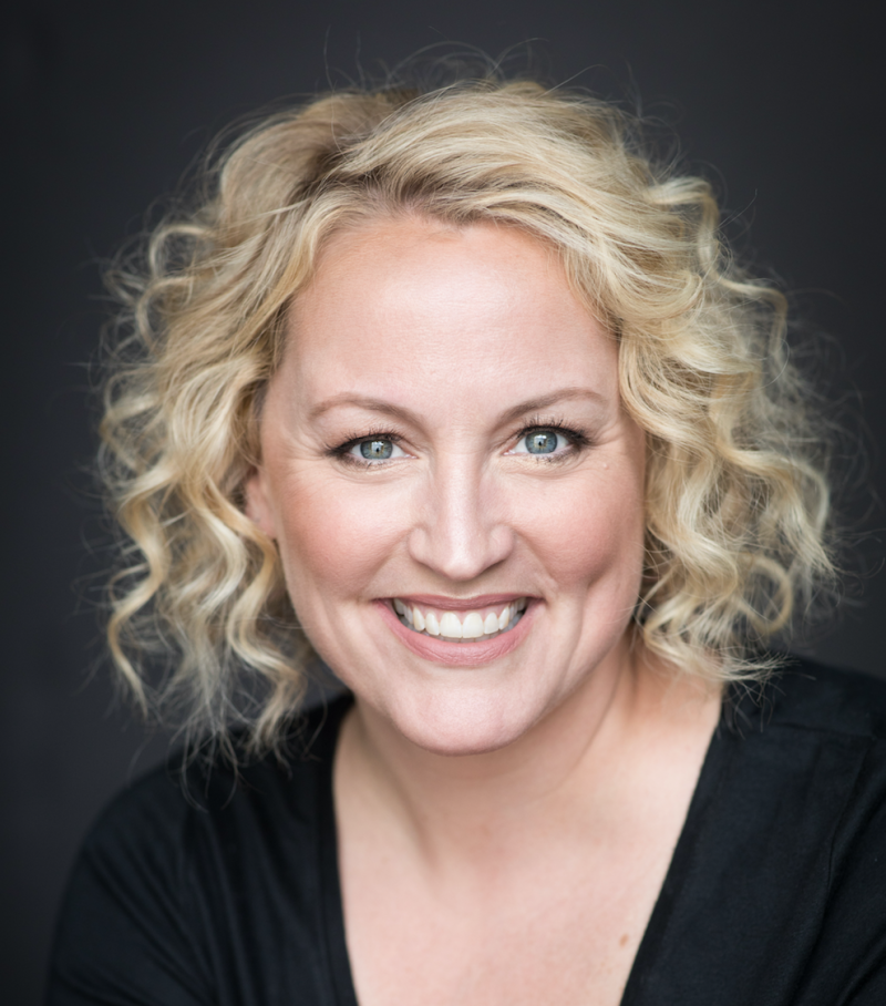 Headshot of woman with blond hair on a dark background.